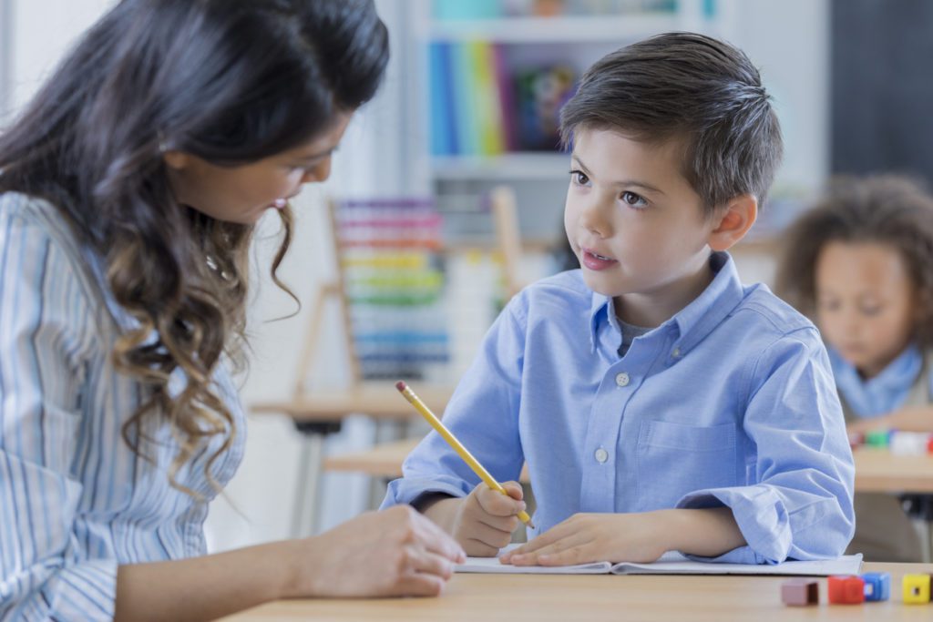 Attentive Asian schoolboy works on a class assignment with his teacher.