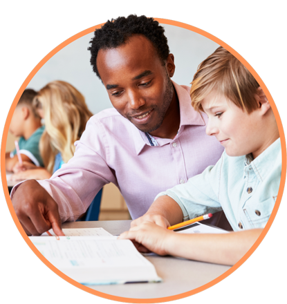 An educator sitting with a young student and pointing at something in a workbook